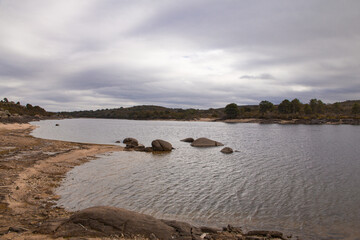 Lake landscape on a cloudy day with forest in the background and shore in the foreground. Soft light. Selective focus.