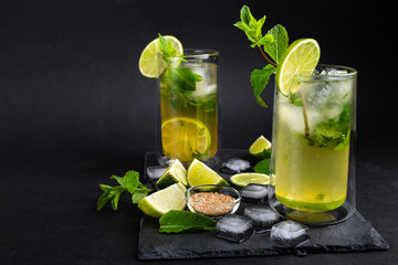 Cold mojito cocktail on the slate board with black background. Refreshing a tasty summer drink full of mint and lime.