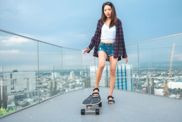 Asian young women surf skate or skates board outdoors on beautiful summer day. Happy young women happy play surf skate  at rooftop city bangkok.