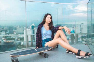 Asian young women surf skate or skates board outdoors on beautiful summer day. Happy young women happy play surf skate  at rooftop city bangkok.