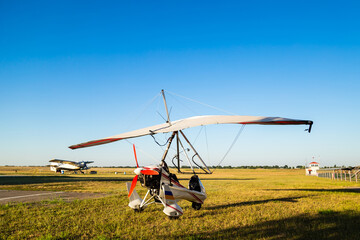 Obraz na płótnie Canvas Motor hang glider standing on green grass at aerodrome, bright summer day