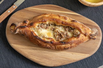 Peinirli with cheese and minced meat crispy baked and ready to serve. Greek open faced pizza on wooden cutting board placed above textile placemat with cutlery.
