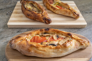 Peinirli with mixed flavours baked and ready to serve. Three Greek open faced pizzas on different cutting boards placed on wooden kitchen surface.