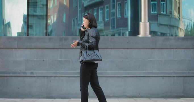 A brunette girl walks past a modern building and talks on the phone. She swears and is in a bad mood. The conversation annoys her. She stops and shouts. Then he drops everything and goes back.