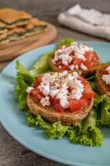Burley rusks with chopped tomatoes and feta cheese served on lettuce leaves. Greek “Dakos” traditional food recipe with greens pie on wooden cutting board - half plate side view.