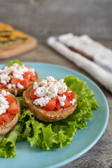 Burley rusks with chopped tomatoes and feta cheese served on lettuce leaves. Greek “Dakos” traditional food recipe - half plate side view.