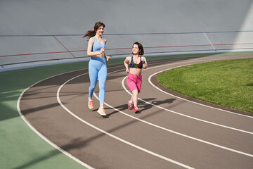 Fototapeta premium Woman running during sunny morning on stadium track with her midget friend