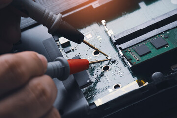 Technician checking laptop circuit board with multimeter