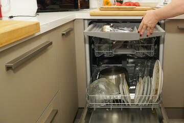 A woman's hand with a manicure loads the dishwasher. An example of saving manicure and female hands using the dishwasher.