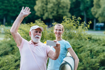 The happy adult sportswoman physiotherapist and elderly bearded man pensioner waving hand making a...