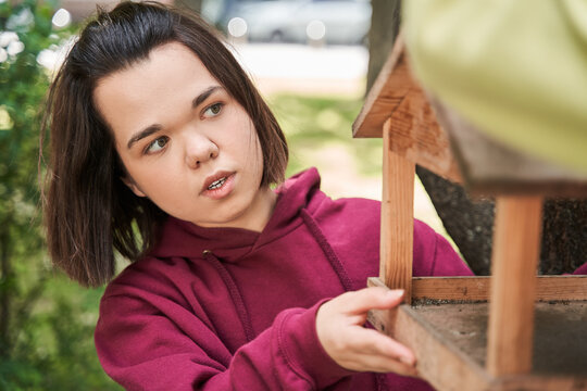 Woman adjusting birds feeder at the tree and preparing to the feeding birds