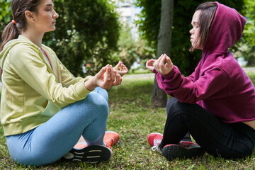 Girls doing yoga exercise at the nature, while sitting in lotus pose at the grass