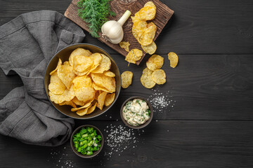 Potato chips with herbs, salt and sour cream on a black background.