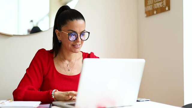 mujer latina senatada en la mesa de su hogar, haciendo negocios desde su laptop