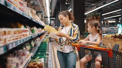 Woman takes packed products from the shelf, packed mushrooms and puts them in a trolley. Little girl and her mom, housewife, enjoy family shopping together - Powered by Adobe