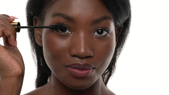 Close up of an african woman's face. Applying mascara on her eyelashes. White background.