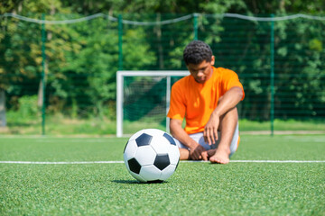 Soccer ball close up against soccer goal and loser sitting on sports field