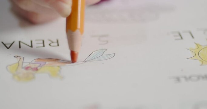 Close up of little girl hands is coloring the drawing of a Mermaid with a black pencil 