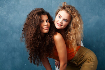 young pretty teenage girls friends with blond and brunette curly hair posing cheerful on blue background, lifestyle people concept