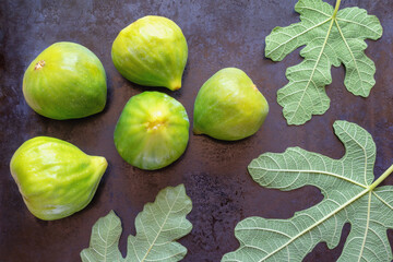 Ripe fig fruit and green leaves of a fig tree on black metal background.  Flat lay