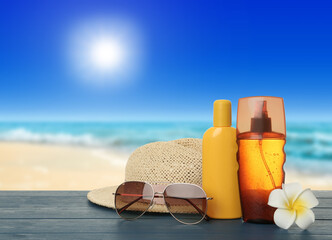 Skin sun protection products and beach accessories on blue wooden table against seascape. Space for...