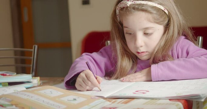 Little girl at home doing homework drawing on school's book with brown pencil