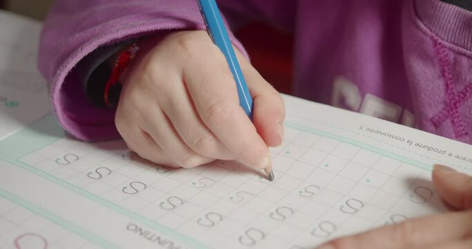 Close-up of a girl's hand learning alphabet writing the letter S on the school's book
