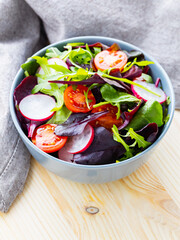 Healthy salad with cherry tomatoes, radish and mix salad. Salad with mix of greens on wooden background. Copy space