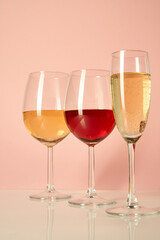 Three glasses of different shapes and containers for wine stand on a white glossy table against a pink background. Glasses with white and red wine