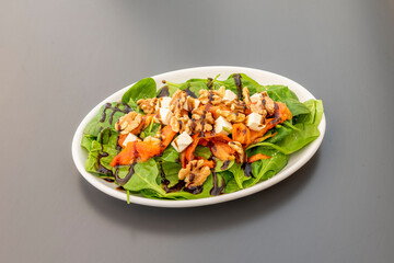 White tray with spinach salad with roasted red peppers, pieces of walnuts, fresh cheese and balsamic of Modena