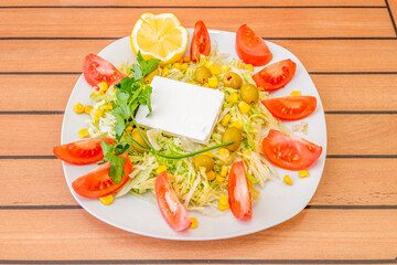 Turkish salad with fresh square cheese, sweet corn, iceberg lettuce with lots of tomato wedges, pitted Spanish olives and a sprig of parsley.
