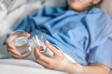 Asian woman patient with medical drip or IV drip holding water with medicine in hospital ward, Selective focus, Healthcare concept.