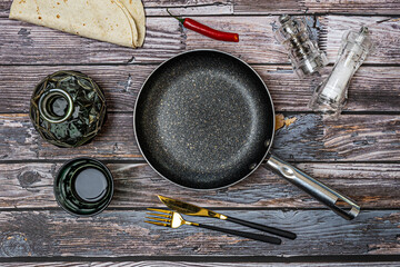 Black frying pan, transparent salt shakers, glass liquor bottle, forks and knives, all on vintage wooden table