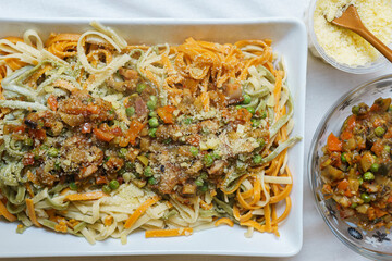 platter with multicolored spaghetti with vegetable sauce and bacon and grated cheese. Top view
