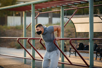 A young man does push-UPS, pull-UPS on a sports field in a mask during a pandemic at sunset. Sports, healthy lifestyle