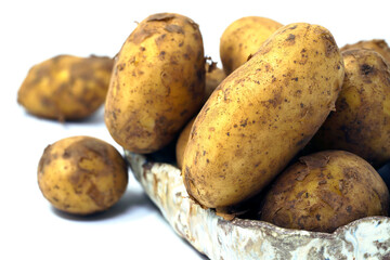 Young potatoes in peel and pieces of earth. Arranged in a ceramic bowl. Two outside. Close up. White background, isolated. 