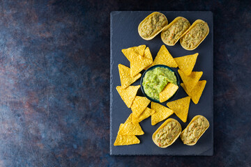 Obraz na płótnie Canvas Mexican guacamole sauce with nachos chips on a slate board. Tortilla chips and guacamole on a dark background. Copy space. Top view