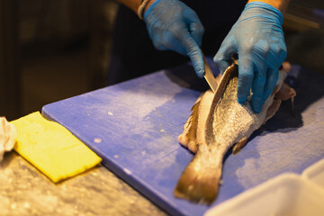 the chef cuts the fish in blue gloves