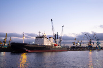 Fototapeta premium Sea ship in cargo port. Cargo ship in port. Loading cranes in background. Transportation of cargo by sea. Ship is waiting for loading of containers in port. Concept - sea logistics.