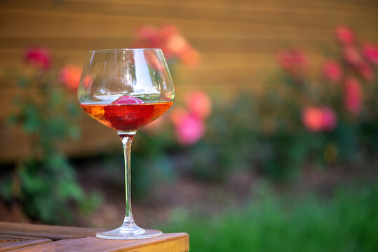 A glass of chilled cold white wine with strawberries on an outdoor wooden terrace