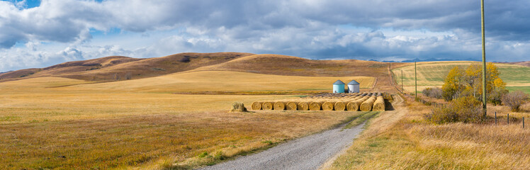 Rural Alberta Canadian prairie grassland landscape countryside background panorama. Beautiful farmer's field and grain silos with hay bales wallpaper  - obrazy, fototapety, plakaty