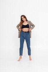 portrait of young caucasian attractive woman with long brown hair in blue jeans, black top and suit jacket on white background. skinny pretty lady posing at studio with bare feet