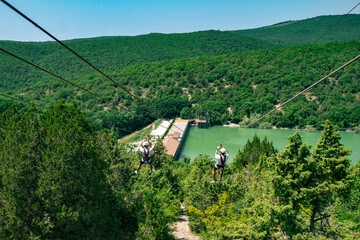 Two guys down a cable in a green valley. Rope descent with a carbine against the backdrop of a huge forest.
