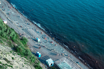 Vacationing tourists on the stone coast of a beautiful sea. A crowd of people resting on the beach near the blue sea.