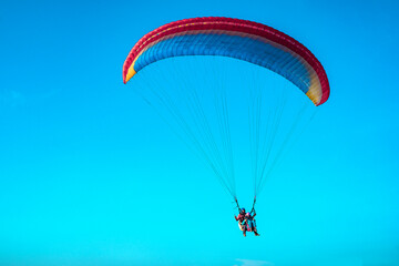 Doubles paragliding against a clear blue sky. A multi-colored papaplan flies in the clear sky closeup.