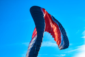 Red-white-blue paraglider filled with the wind close-up. A multi-colored wing of a paraglider against a clear sky. Paraglider in the sunlight against the blue sky.