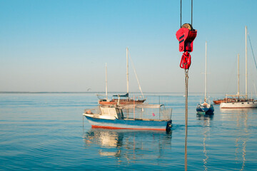 Red cargo hook in the port against the background of yachts and boats in the marina.
