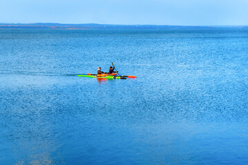 A company of young people on kayaks is training at sea. A pair of multi-colored canoes sail in the blue sea. Spring canoeing guy and girl in the lake
