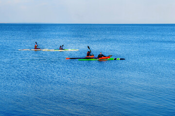 A company of young people on kayaks is training at sea. Four multi-colored canoes sail in the blue...