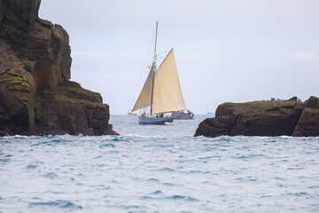 Tall yacht sailing between rocks at sea in the Isles of Scilly - 444478998